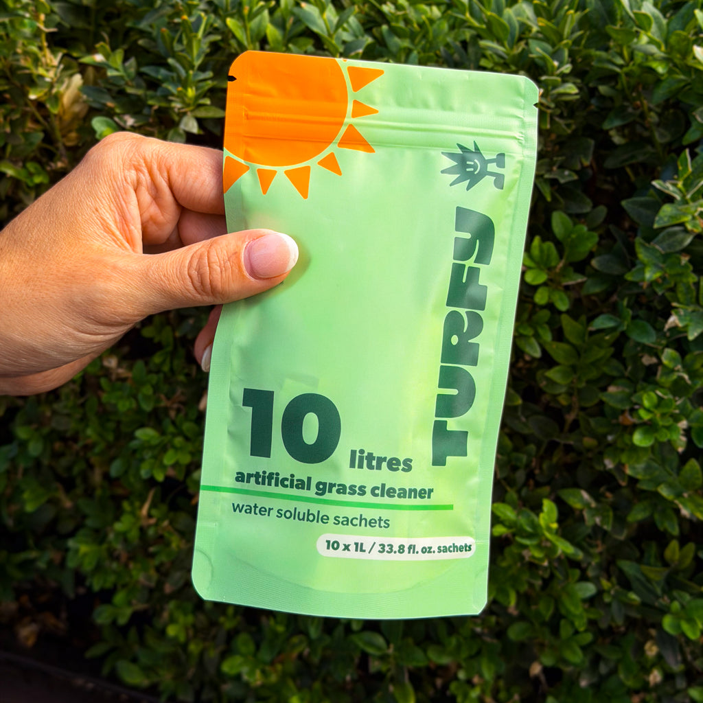 A hand holding a small, dissolvable Turfy probiotic sachet in front of a lush green backyard, showing the compact size of our powerful cleaner.